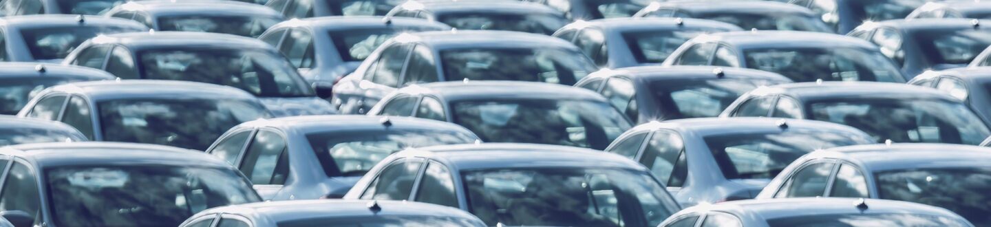 Rows of a new cars parked in a distribution center on a car factory on a sunny day. Top view to the parking in the open air. - Dealership Landing Page