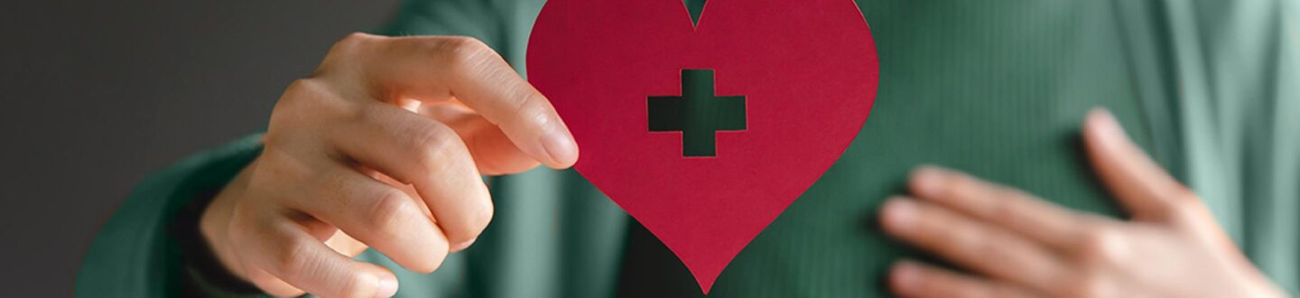 Woman in a green sweater holding up a red paper heart - Nonprofit Audit and Accounting Services